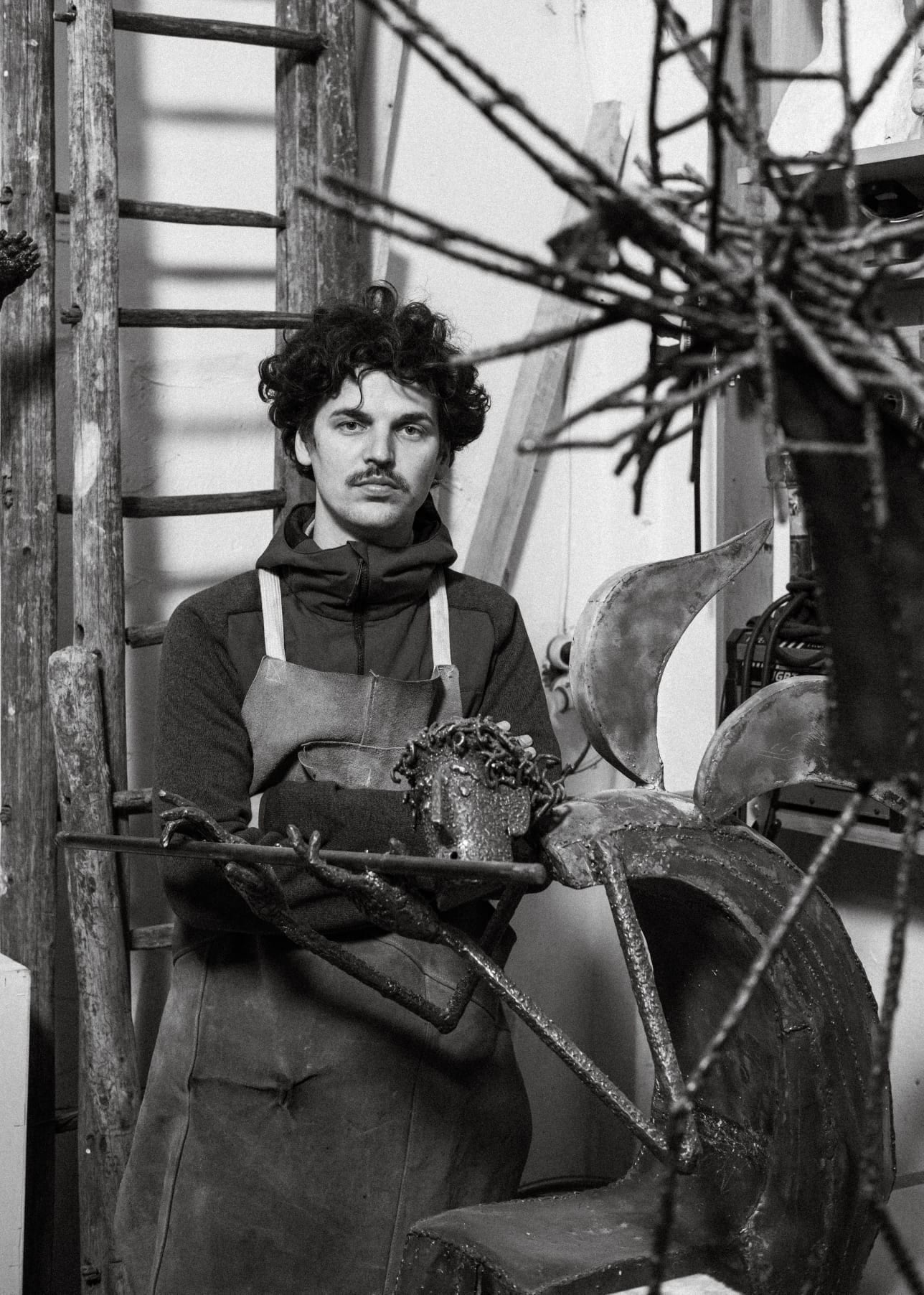 Emanuel Chiriac purtând șorț de atelier, alături de o sculptură în lucru